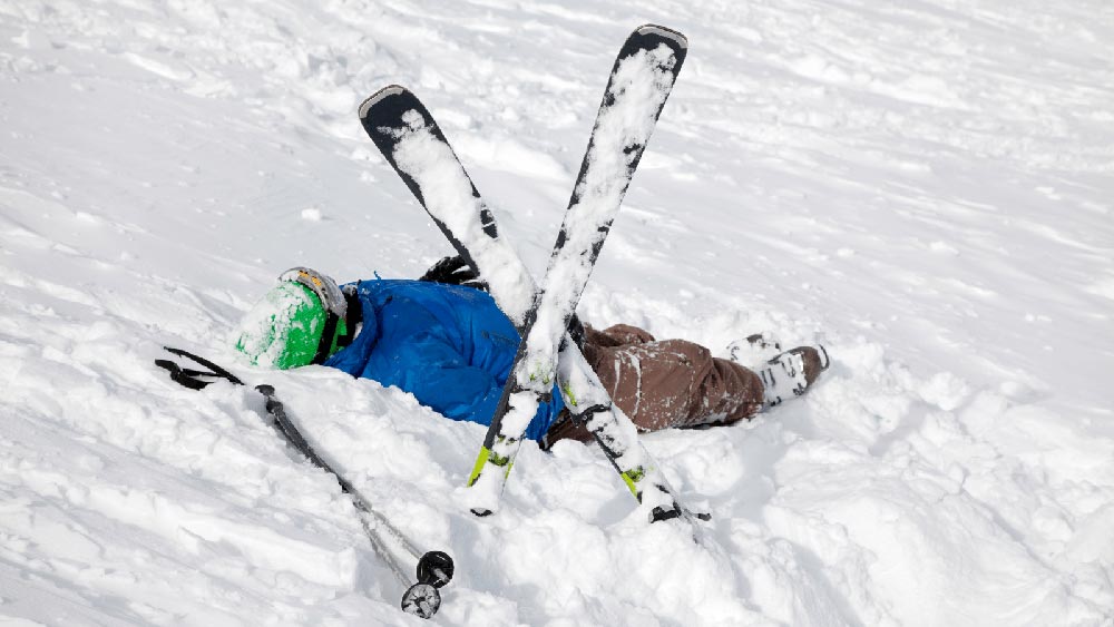 A person lying in the snow after a ski accident with their skis crossed so that other skiers know they are injured.