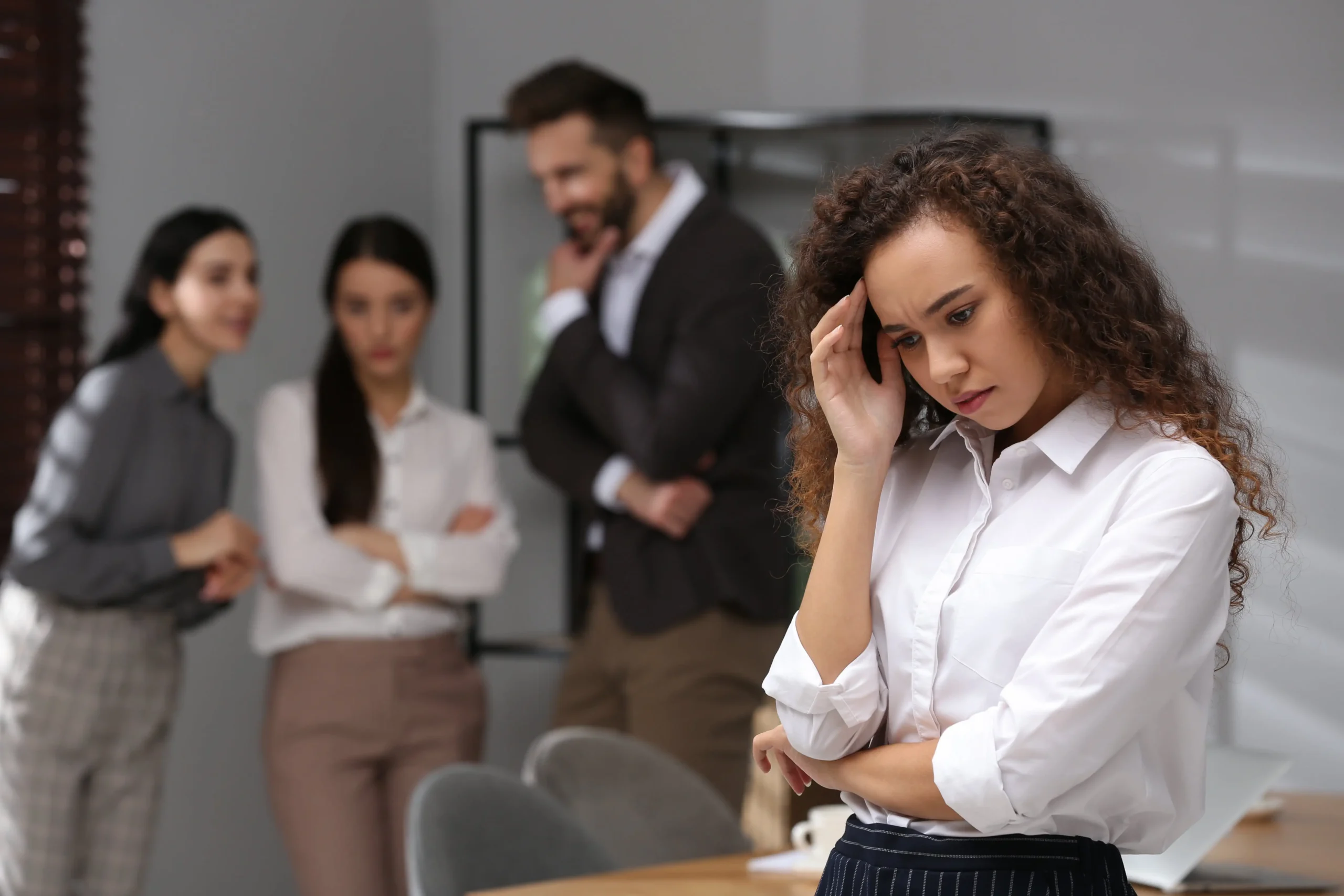 A businesswoman stands apart looking distressed, illustrating workplace discrimination in a Denver office."